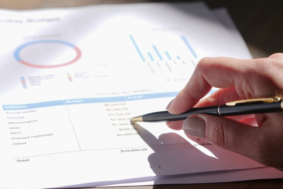 Hand holding a pen while analyzing a budget on graph paper with charts